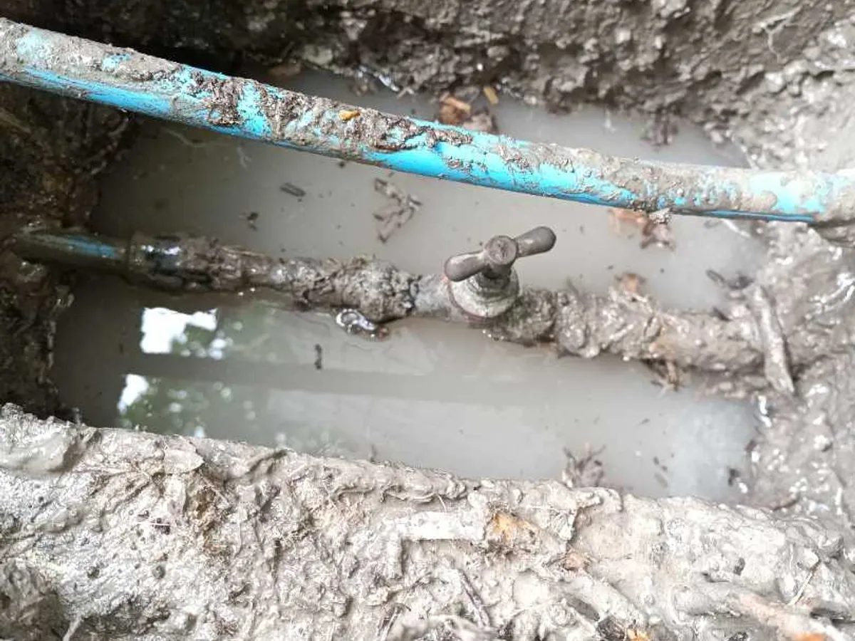 A blue MDPE supply pipe and its buried stop valve exposed in a waterlogged excavation